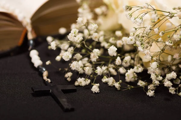 Закрыть четки над святой библией с размытыми белыми маленькими цветами, черный фон — стоковое фото