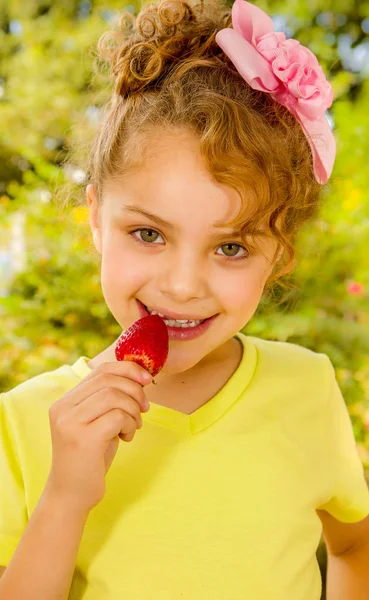 Bir bahçe arka planda sağlıklı bir çilek yeme sarı bir tişört giyen güzel genç kız — Stok fotoğraf