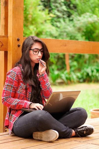 Cool hipster student kvinna som bär glasögon glasögon. Kaukasiska kvinnliga universitetsstudent söker och hennes dator i utomhus, bakgård bakgrund — Stockfoto