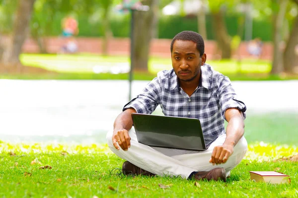 Joven hombre negro sentado sobre hierba verde y trabajando en su computadora en la ciudad de Quito Ecuador — Foto de Stock