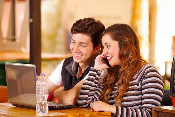 Schönes Paar an der Bar, das Zeit miteinander verbringt, während er an seinem Computer arbeitet, während sie ihr Handy benutzt — Stockfoto