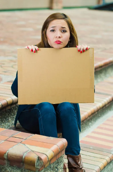 Mujer joven con ropa casual sentada al aire libre sosteniendo cartel de cartón, protestando concepto —  Fotos de Stock