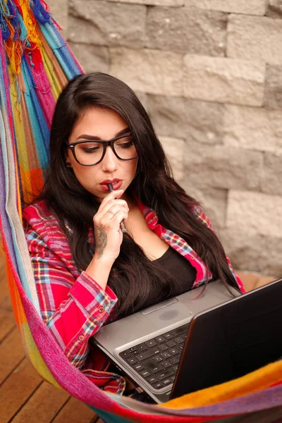 Linda hipster relaxante e deitado em uma rede colorida e desfrutar da vida, usando seu celular e computador — Fotografia de Stock