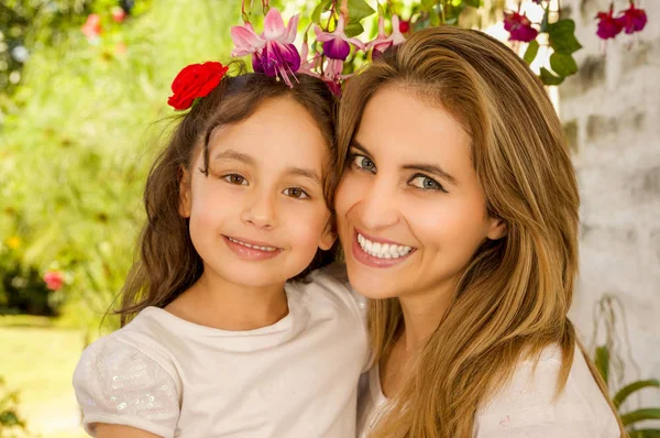 Sonriendo hermosa mamá abrazando a su bonita hija en vestido beige con dos corbatas rojas en el pelo — Foto de Stock