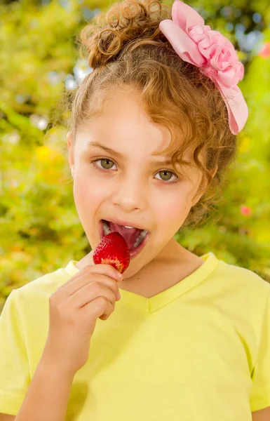 Bir bahçe arka planda sağlıklı bir çilek yeme sarı bir tişört giyen güzel genç kız — Stok fotoğraf