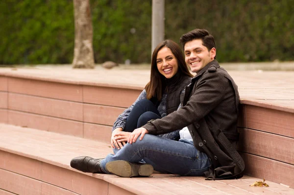 Primer plano de una hermosa joven pareja sonriente enamorada en San Valentín y mirando a la cámara, sentada en un parque —  Fotos de Stock