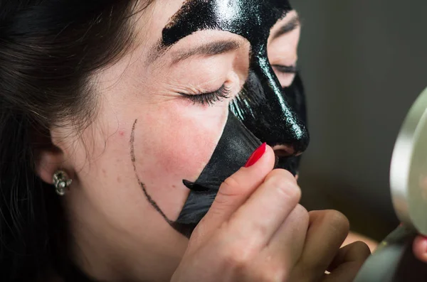 Primo piano di una giovane donna di bellezza che toglie metà di una maschera nera guardando lo specchio — Foto Stock