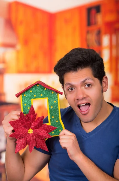 QUITO, ECUADOR- 17 OCTOBER, 2015: Close up of a surprised handsome young man holding in his hand a christmas tree decoration in a blurred background — Stock Photo, Image