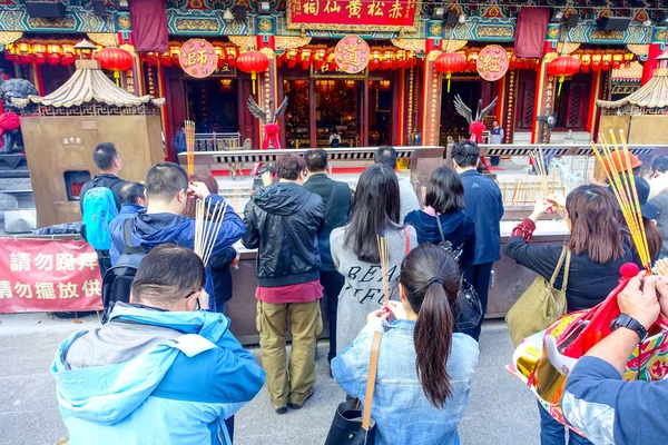 HONG KONG, CHINA - 22 DE ENERO DE 2017: Multitud de personas sosteniendo sus manos con palos de incienso y rezando dentro del templo budista Wong Tai Sin para orar, en Hong Kong, China —  Fotos de Stock