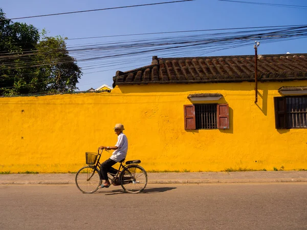 ホイアン、ベトナム - 2017 年 8 月 5 日: 正体不明の男の古代の町、世界遺産ホイアンの古い黄色い家の前で自転車に乗る。ホイアン、ベトナムで最も人気のある目的地の一つです — ストック写真