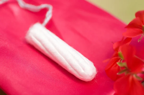 Close up of a a menstruation cotton tampon over a red cotton bag, with a beautiful red flower, in a blurred background — Stock Photo, Image