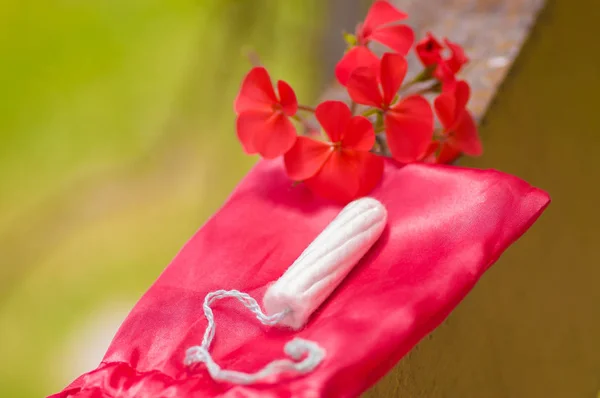 Primer plano de un tampón de algodón menstruación sobre una bolsa de algodón rojo, con una hermosa flor roja, en un fondo borroso —  Fotos de Stock