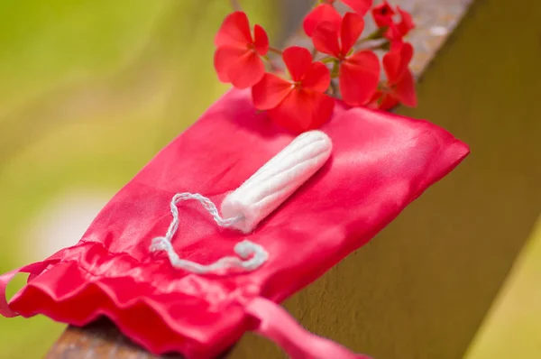 Крупный план менструации хлопкового тампона поверх красного хлопкового мешка, с красивым красным цветком, на размытом фоне — стоковое фото