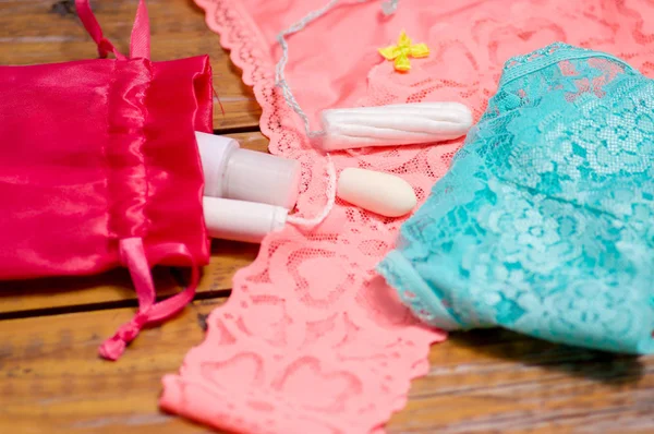 Close up of a a menstruation cotton tampon and an ovum, over a pink and blue woman underwear, and red cotton bag, in a wooden table, in a blurred background — Stock Photo, Image