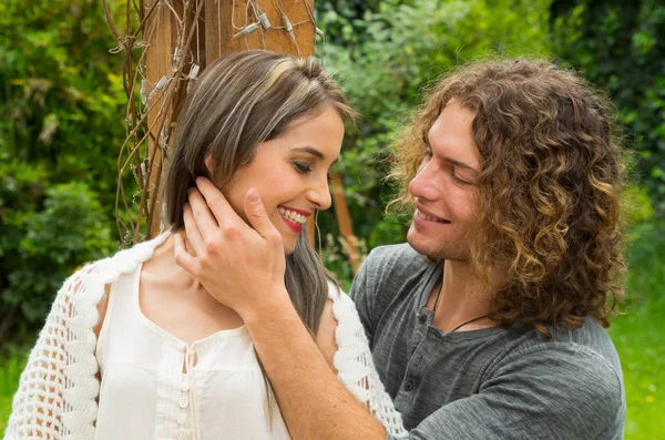 Couple heureux amoureux à l'extérieur et souriant, homme aux cheveux bouclés touchant le visage de sa petite amie dans un arrière-cour patio — Photo