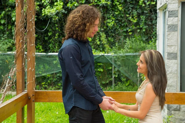 Couple heureux en amour à l'extérieur et en se regardant, femme sur ses genoux et tenant ses mains de petit ami, dans un fond de patio arrière-cour — Photo