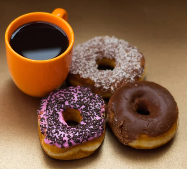 Крупним планом смачні пончики з шоколадом, кокосовою і рожевою глазур'ю з деякими чіпсами шоколаду, з апельсиновою чашкою кави на дерев'яному фоні, вид зверху — стокове фото