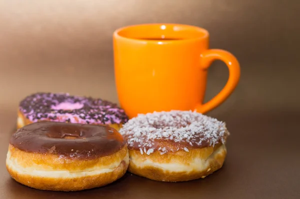 Смачні пончики з шоколадом, кокосовим горіхом і рожевою глазур'ю з деякими чіпсами шоколаду, з апельсиновою чашкою кави на дерев'яному фоні — стокове фото