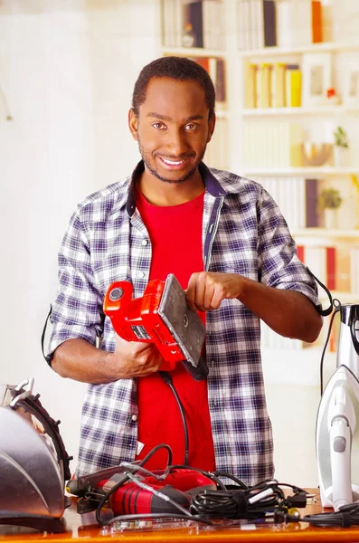 Glücklich junge afrikanische ecuadorianische männliche Techniker Reparatur eines roten Schleifers mit seinem Schraubendreher auf Bürohintergrund — Stockfoto