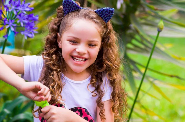 Happy little curly smiling girl playing with soap bubbles on a summer nature, wearing a blue ears of tiger accessories over her head in a blurred nature background — Stock Photo, Image