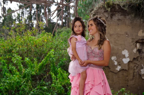 Mulher bonita e sua filhinha bonita olhando uns aos outros e sorrindo, vestindo um vestido de princesa rosa ao ar livre — Fotografia de Stock