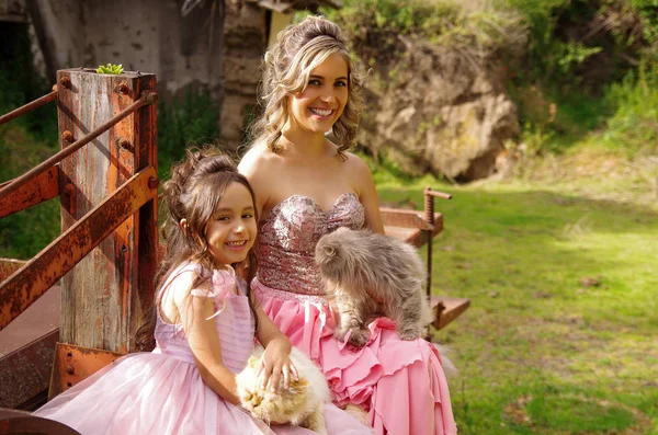 Schöne Frau und ihre süße kleine Tochter, die in die Kamera schaut und lächelt, in einem Prinzessinnenkleid, während sie ihre Katzen im Freien umarmen — Stockfoto