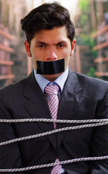 Arka plan bulanık içinde onun ağız içinde siyah bant ile işadamı ip, sandalyeyle tuzak