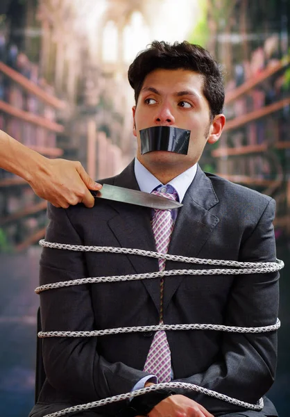 Siyah bir bant içinde onun ağız, korkmuş-in onun neack yakınındaki bir bıçağı bulanık bir arka planda tutan bir el ile işadamı ip, sandalyeyle tuzak