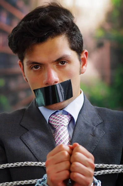 İp, sandalyeyle siyah bir bant içinde onun ağız ve arka plan bulanık elinde bir zincir ile sıkışmış bir işadamı yakın çekim