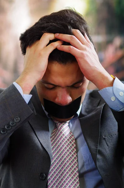 Empresário com uma fita preta na boca, e tocando seu cabelo com desespero, em um fundo embaçado — Fotografia de Stock