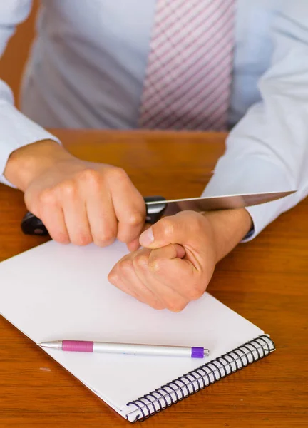 Close up of a man wants to commit suicide, using a knife in his wrist, over a notebook with a pen in a wooden table, wooden background — Stock Photo, Image