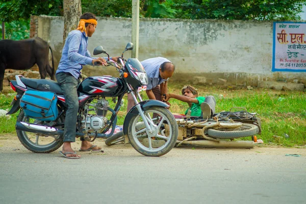 AGRA, INDIA - 19 DE SEPTIEMBRE DE 2017: Un hombre no identificado monta una motocicleta, mientras que otro hombre está ayudando a su amigo que se cayó de su motocicleta, en las calles del centro de la India en Agra, India — Foto de Stock