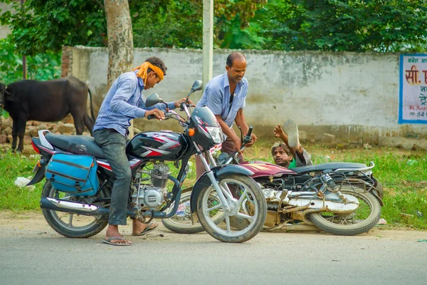 AGRA, INDIA - SEPTEMBER 19,M 2017: Unidentified man rides a motorcycle, while other man is helping his friend that felldown from his motorcycle, in the streets in central India in Agra, India — Stock Photo, Image