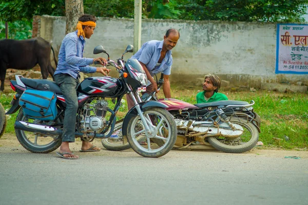 AGRA, INDIA - 19 DE SEPTIEMBRE DE 2017: Un hombre no identificado monta una motocicleta, mientras que otro hombre está ayudando a su amigo que se cayó de su motocicleta, en las calles del centro de la India en Agra, India — Foto de Stock