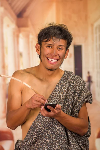 Primer plano de divertida sonrisa prehistórica a la cámara, sosteniendo un teléfono celular y escribiendo con un palo de madera, en un fondo borroso —  Fotos de Stock