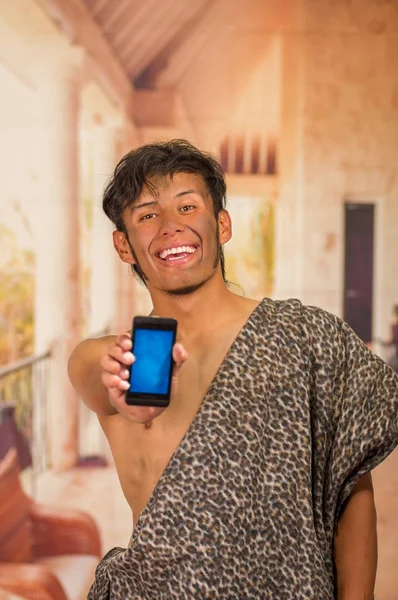 Close up of funny prehistoric man smiling to the camera, and pointing his cellphone in front, in a blurred background