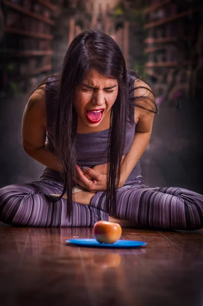 Vacker och ensam tjej som lider av anorexy, lider av smärta i magen när hon ser ett äpple över en blå tallrik, i en suddig bakgrund — Stockfoto