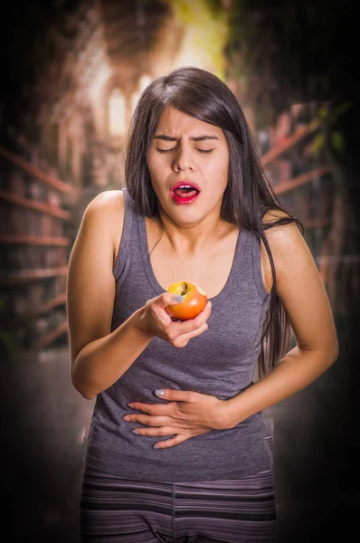 Vacker och ensam tjej lider anorexy, lider av smärta i magen när hon ser ett äpple och gör äckliga ansikten, i en suddig bakgrund — Stockfoto