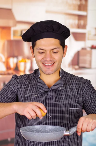 Улыбающийся парень держит сковородку на кухне с яйцом в руке, готовит блюдо, чураско экваториальной кухни — стоковое фото