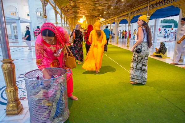 新德里，印度-2017 年 9 月 19 日： 身份不明的人走在广场在绿色的地毯上，与女人存款塑料桔在金属 trasin 著名的锡克教谒师所金殿 — 图库照片