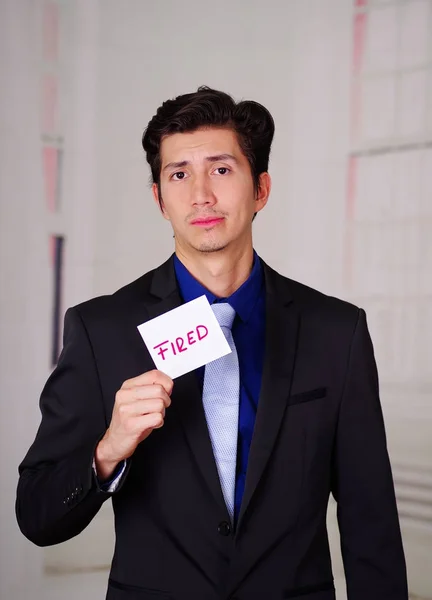 Sad business man holding a paper of fired text on it in his hand, in a blurred background