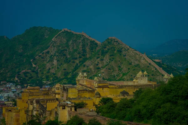 Beautiful view of yellow castle of Amber Fort with green trees, mountains and small houses near Jaipur in Rajasthan, India. Amber Fort is the main tourist attraction in the Jaipur area