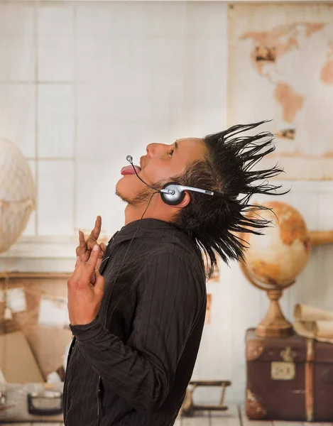 Close up of office punk man wearing a suit with a crest, wearing aheadphones, and doing a sign with his hands and sticking out the tongue, in a blurred background — Stock Photo, Image