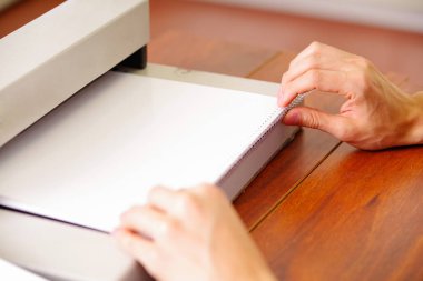 Adam ahşap bir masa üzerinde bir plastik telli makine kullanarak belgeleri bağlama için ellerini kullanarak belgeleri düzenleme