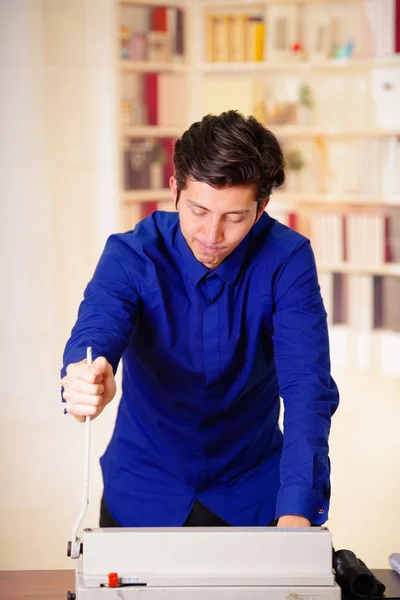 Primer plano del joven guapo usando una camiseta azul usando una palanca para encuadernación de documentos con aglutinante de anillo de plástico mediante el uso de la máquina de encuadernación de anillo — Foto de Stock