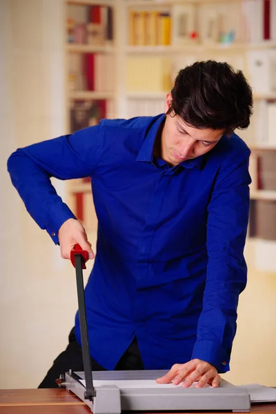 Gros plan d'un beau jeune homme portant un t-shirt bleu à l'aide d'un levier pour relier des documents avec un liant à anneaux en plastique en utilisant une machine à relier les anneaux — Photo