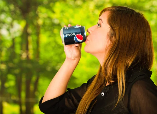 Quito, Ecuador May, 06, 2017: Pretty young woman drinking a pepsi in blurred green background — Stock Photo, Image