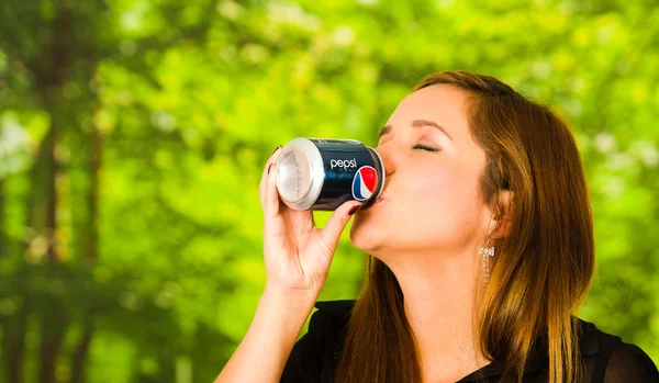 Quito, Ecuador 06 maggio 2017: Ritratto di una bella giovane donna che beve un pepsi su sfondo verde sfocato — Foto Stock