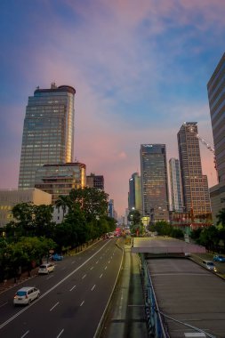 Jakarta, Endonezya - 3 Mart, 2017: Modern şehir manzarası parçası mesafeden, mor renkli güzel günbatımı gökyüzü görüldüğü gibi ışık trafik önünde geçen