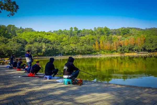 SHENZEN, CINA - 29 GENNAIO 2017: All'interno del parco Lian Hua Shan, ampia area ricreativa, persone sedute a pescare nel lago d'acqua circondate da alberi, bellissimo cielo blu , — Foto Stock